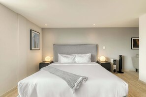 Ein modernes Hotelzimmer mit einem großen Bett, zwei Nachttischen mit Lampen, einem Heizkörper und einem Sessel.
