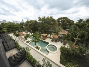 Un área de piscina en la azotea con jacuzzi, sillas de descanso y palmeras.
