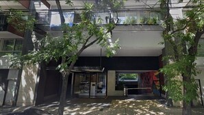 Ein modernes Gebäude mit Glastür, einem Balkon und einem Baum im Vordergrund.