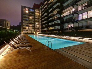 Ein Poolbereich mit Liegestühlen und einem Schwimmbecken, umgeben von mehrstöckigen Gebäuden mit Balkonen.