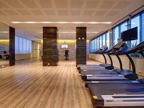 Ein Fitnessraum mit Laufbändern, Rudergerät und Wandfernseher.