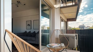 Ein Balkon mit Korbstuhl, Glastisch und einer Couch im Hintergrund.
