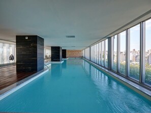 En indendørs swimmingpool med udsigt til bylandskab gennem store vinduer.