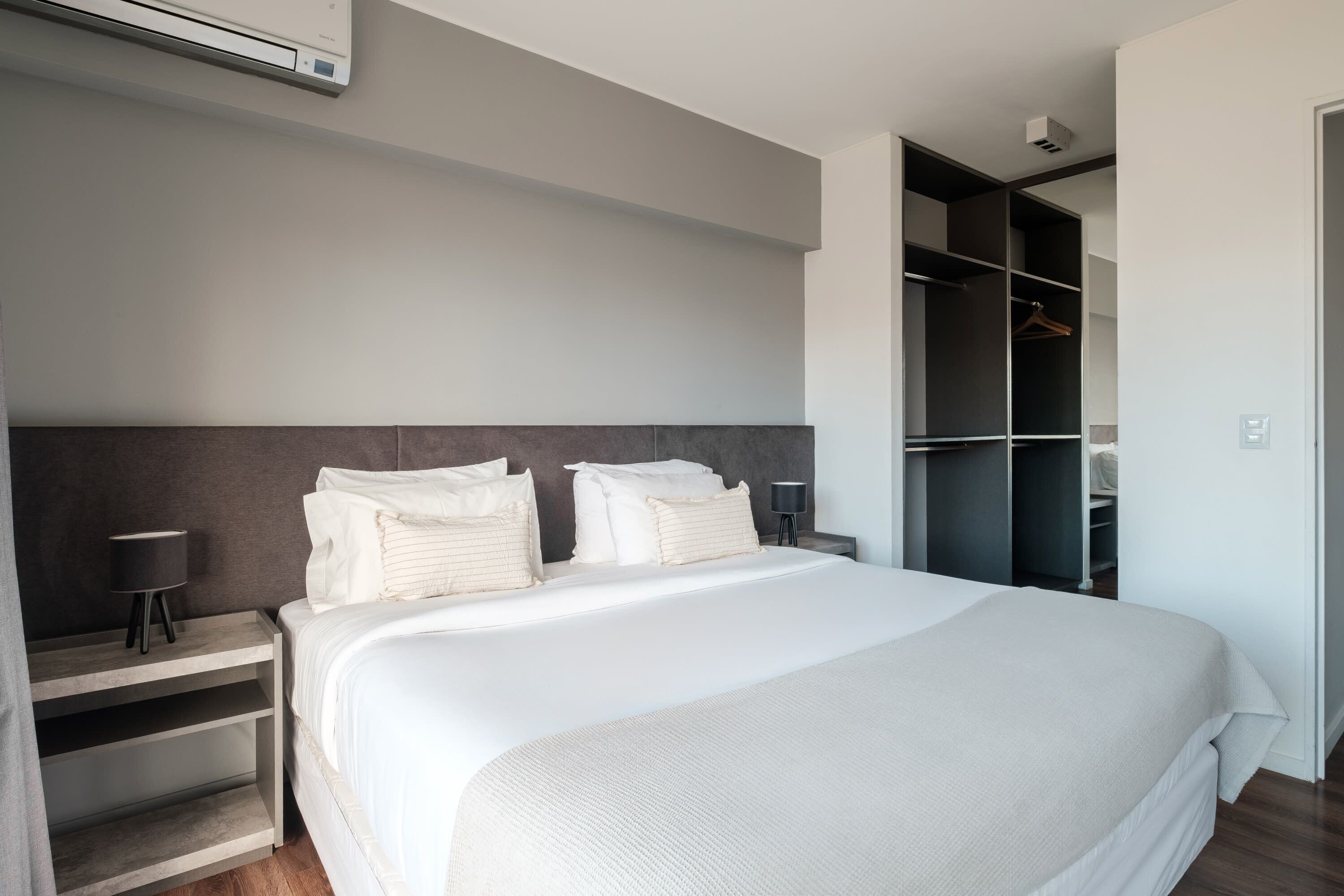 Ein modernes Hotelzimmer mit einem großen Bett, Nachttischen, einem Kleiderschrank und einer Klimaanlage.