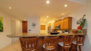 A kitchen with wooden cabinets, a granite countertop, and four bar stools. - Del Mar 4G - 3 bdr 2 bath (Playa Herradura)