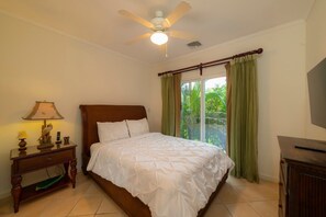 A bedroom with a bed, a nightstand with a lamp, a ceiling fan, and a view of greenery outside. - Del Mar 4G - 3 bdr 2 bath (Playa Herradura)