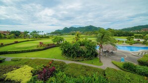 A golf course with a pool area, lush greenery, and distant hills. - Del Mar 4G - 3 bdr 2 bath (Playa Herradura)