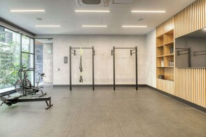 Ein Fitnessraum mit Trainingsgeräten, einer Klimmzugstange und einem Fenster mit Blick auf Grünflächen.