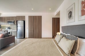 A modern bedroom with a large bed, a sofa, and a kitchen in the background. - Chic Central Park Studio (Ciudad de México)