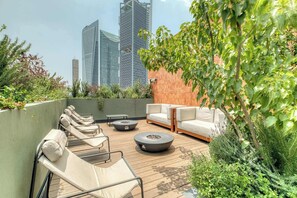 Terraço no telhado com cadeiras de descanso, lareira e vista para edifícios altos.