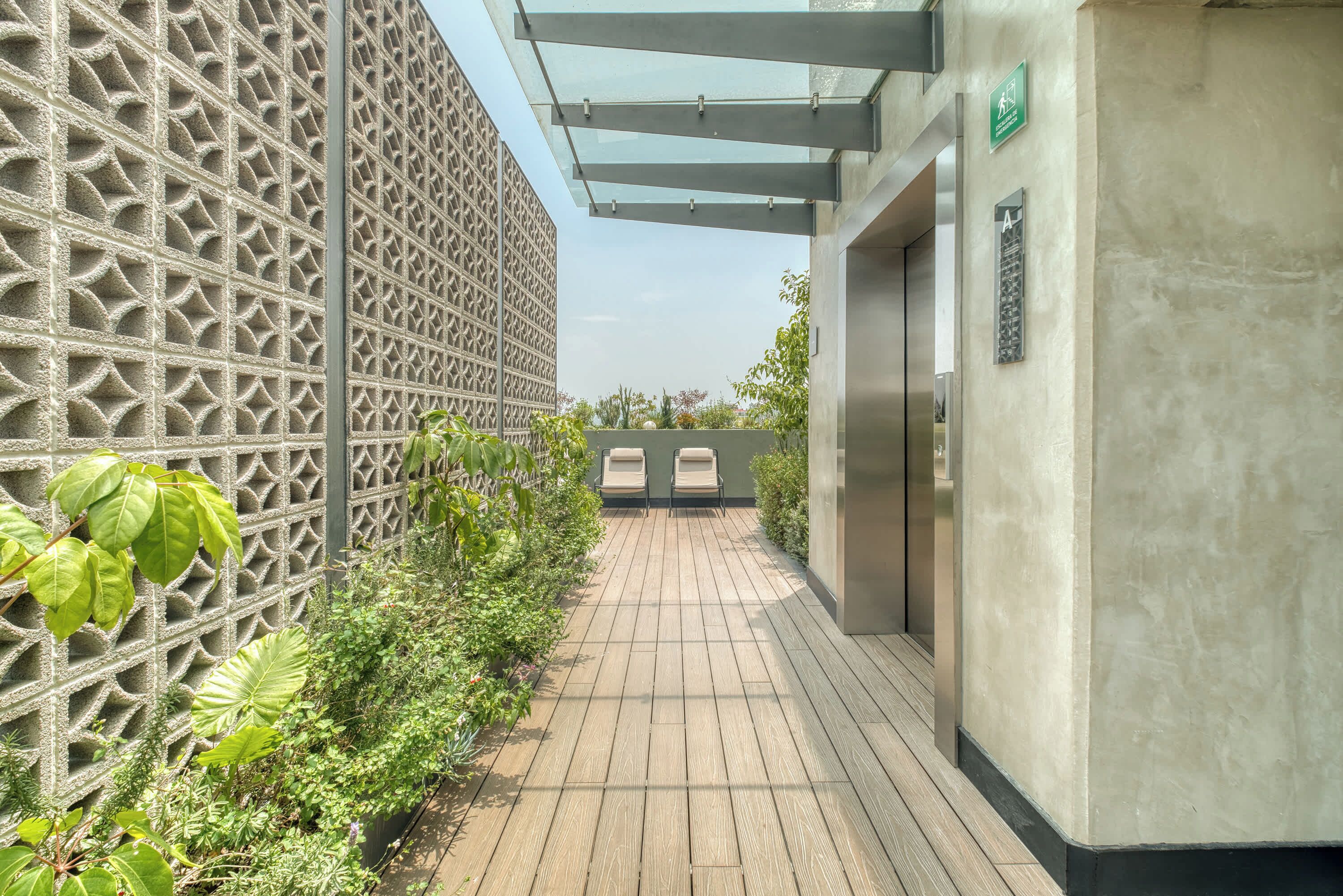 A corridor with a patterned wall, a wooden floor, and a glass ceiling structure.