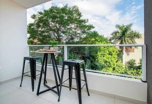 A balcony with two black stools, a small table, and a glass railing. - Chic 1BR, Work Desk w/ Pool&Gym (Asunción)