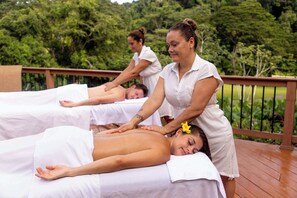 Un espace dédié aux massages, où trois clients reçoivent des soins sur une terrasse en bois offrant une vue sur une végétation luxuriante.