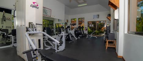 A gym with various exercise machines, a ceiling fan, and large windows.