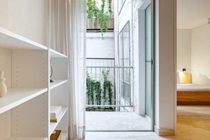 A modern interior with white shelving, a glass door leading to a balcony with plants, and a wooden floor. - CAM 1-Bdrm w Balcony (Ciudad de México)
