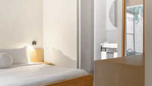 Ein Schlafzimmer mit einem hölzernen Bett, einem Nachttisch mit Lampe und Blick auf ein Badezimmer durch eine Glastür.