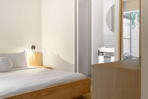 Ein Schlafzimmer mit einem hölzernen Bett, einem Nachttisch mit Lampe und Blick auf ein Badezimmer durch eine Glastür.