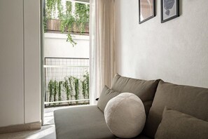 A modern living room with a sofa, a round cushion, and a view of a balcony with plants. - CAM 1-Bdrm w Balcony (Ciudad de México)