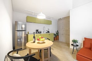 Eine kompakte Küche mit Essbereich, einem modernen Kühlschrank und einem kleinen Tisch mit Früchten und einer Flasche.