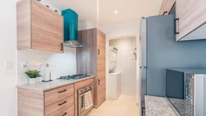 A modern kitchen with wooden cabinets, a gas stove, and a built-in oven. - Cozy 1br with Balcony, Pool & Beach Access Cap Cana (Punta Cana)