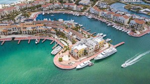 An aerial view of a marina with boats docked, surrounded by residential buildings with red roofs. - Cozy 1br with Balcony, Pool & Beach Access Cap Cana (Punta Cana)