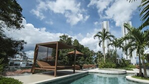 Una piscina con una estructura de sombrilla, sillas de descanso y palmeras.