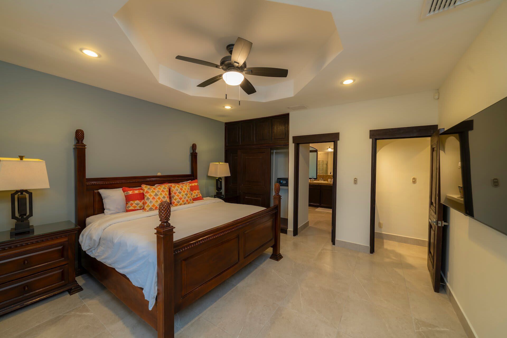 A bedroom with a bed, nightstands, a ceiling fan, and a bathroom visible through an open door.