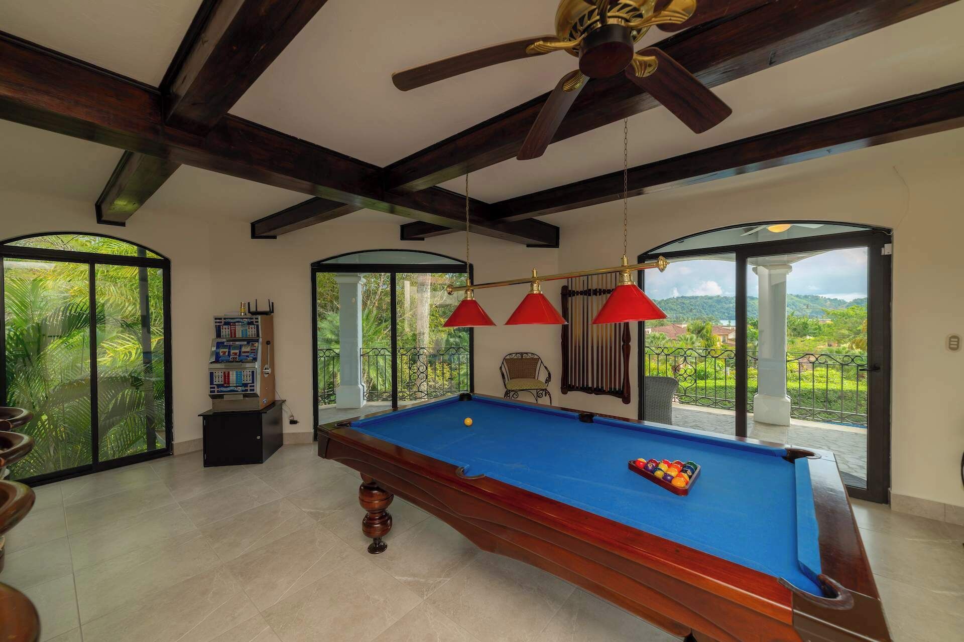 A pool table with a blue felt surface, red hanging lamps, and a ceiling fan.