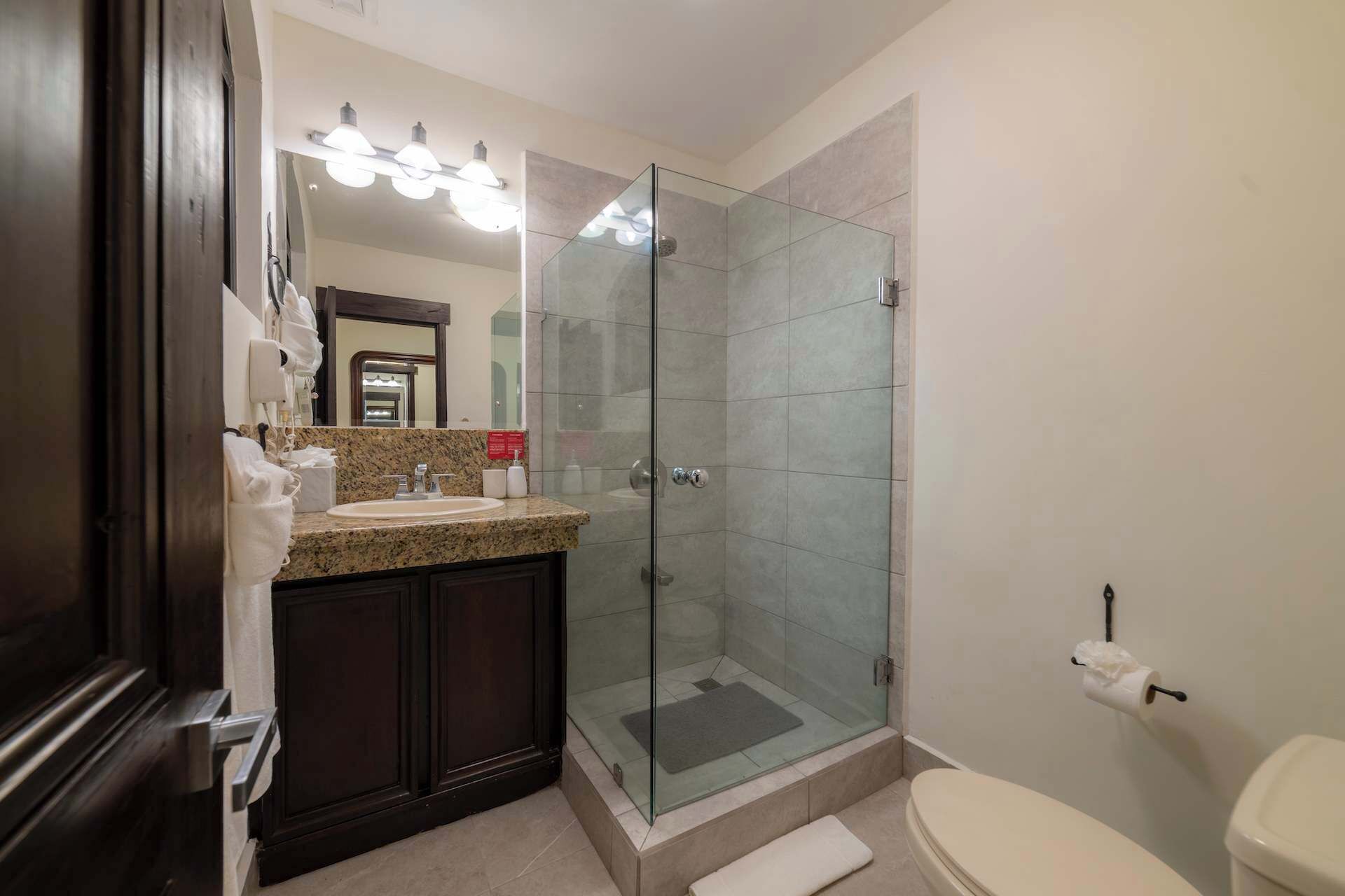 Un baño con ducha de vidrio, lavamanos de granito y retrete.
