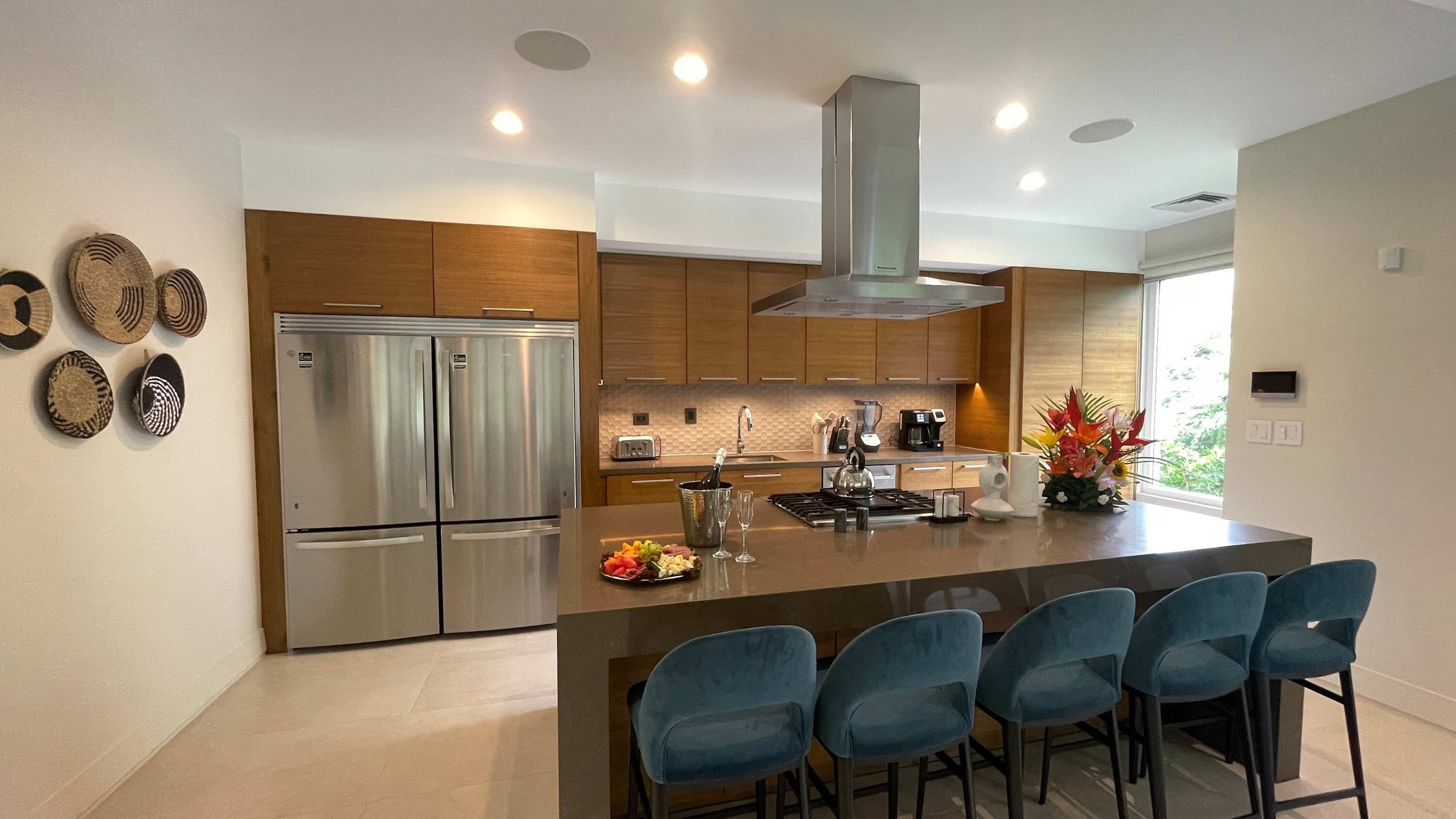 A modern kitchen with a central island, bar stools, stainless steel appliances, and wooden cabinetry.