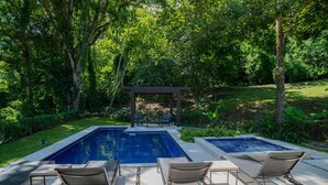 Uma piscina retangular com hidromassagem, cercada por espreguiçadeiras e um pergolado.