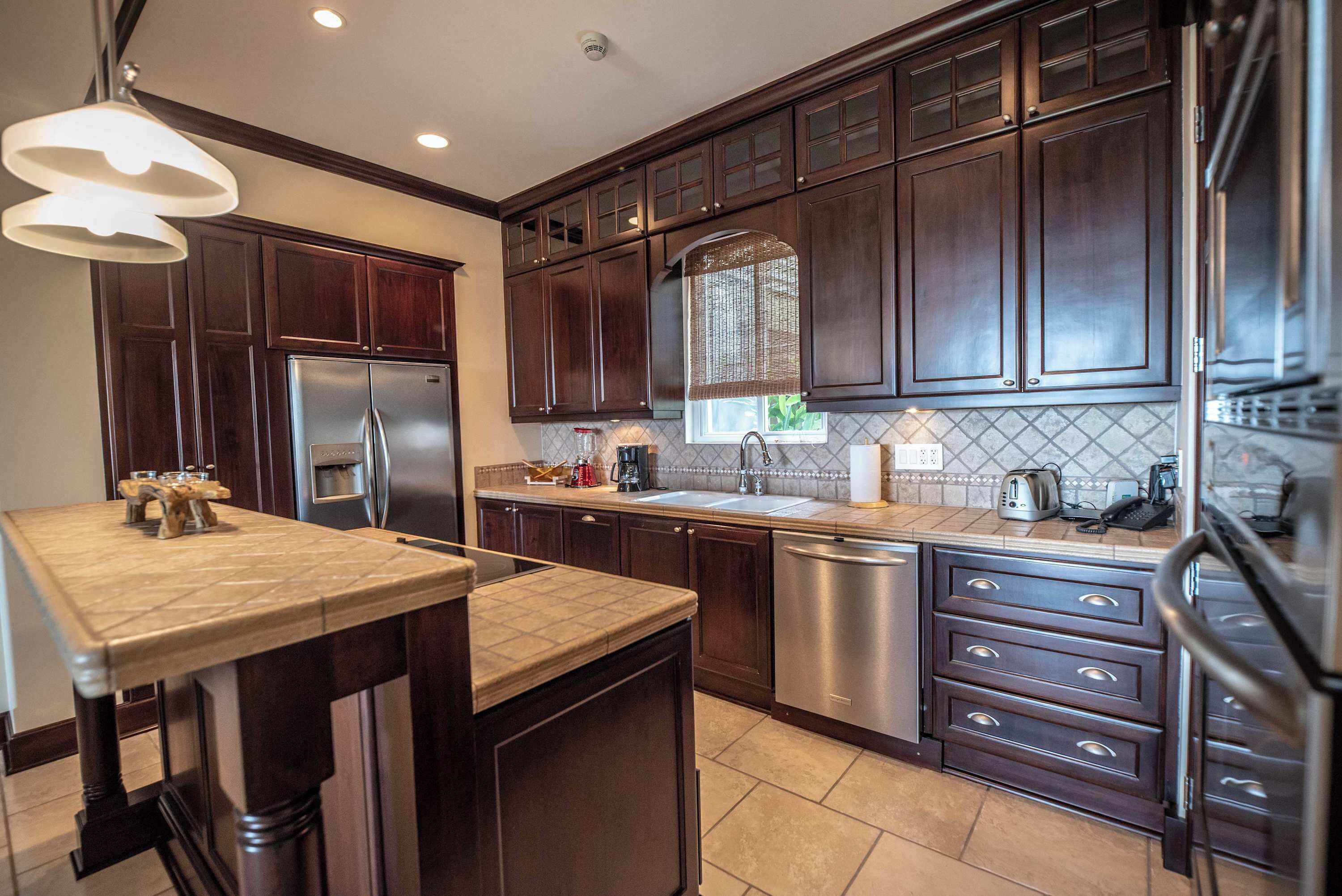A modern kitchen with dark wood cabinets, stainless steel appliances, and a large island with a light fixture.