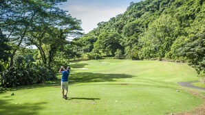 A golf course with a person preparing to take a shot, surrounded by lush greenery and trees. - Montebello 1E 3 bed 3 bath, ocean view (Playa Herradura)