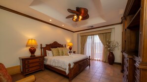 A hotel room with a wooden bed, two bedside lamps, a ceiling fan, a large window with curtains, and a wooden dresser. - Montebello 1E 3 bed 3 bath, ocean view (Playa Herradura)