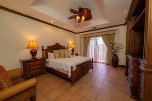 A hotel room with a wooden bed, two bedside lamps, a ceiling fan, a large window with curtains, and a wooden dresser. - Montebello 1E 3 bed 3 bath, ocean view (Playa Herradura)