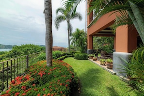 A landscaped outdoor area with a pathway, palm trees, and a view of a body of water. - Montebello 1E 3 bed 3 bath, ocean view (Playa Herradura)