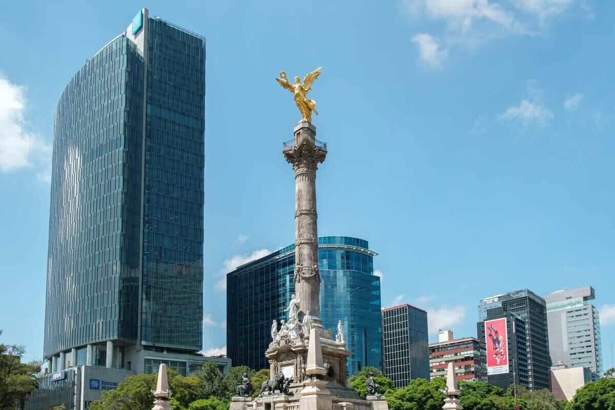 Un moderno horizonte urbano con una prominente estatua dorada sobre una columna en primer plano.