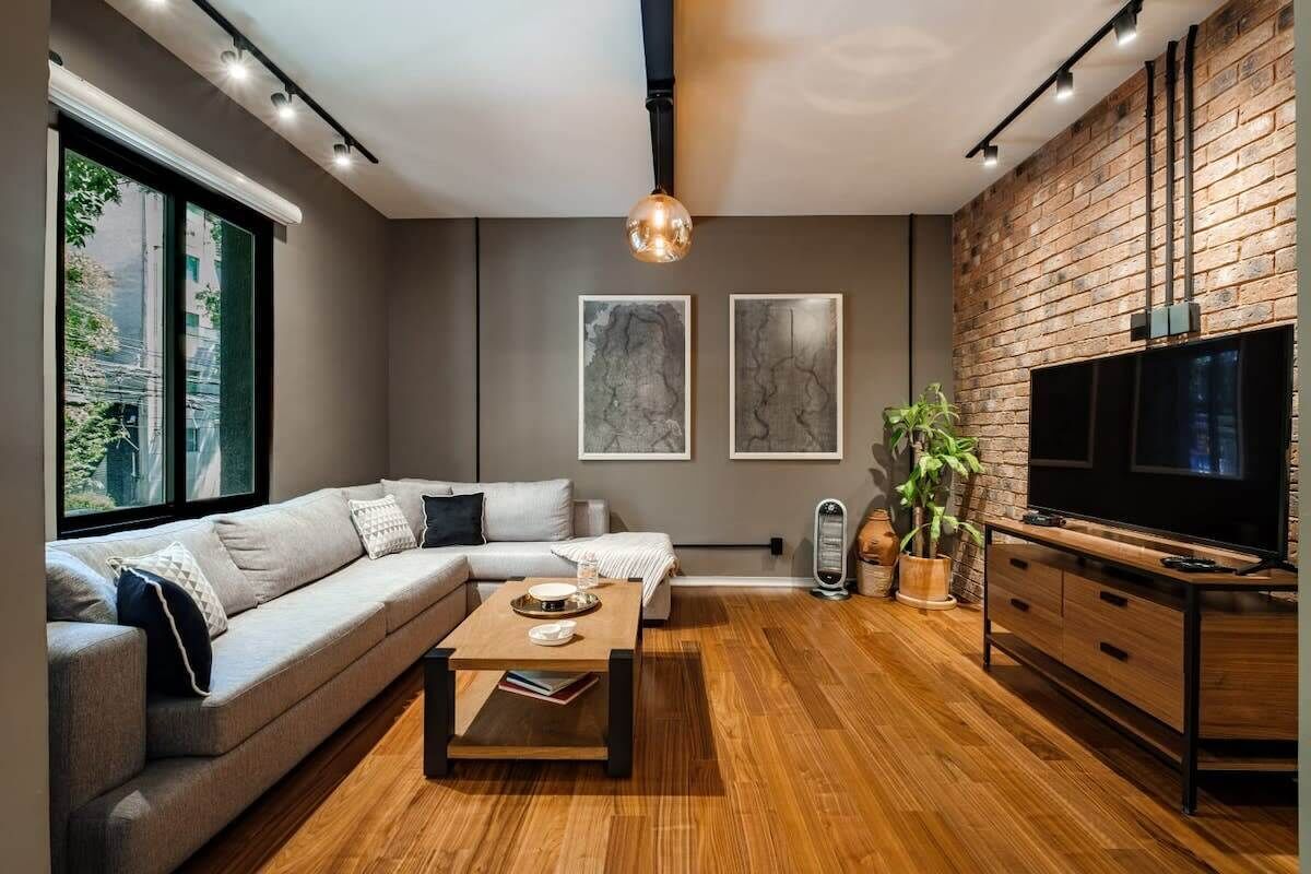 Una sala moderna con un sofá seccional, una mesa de centro, un televisor y una pared de ladrillo.