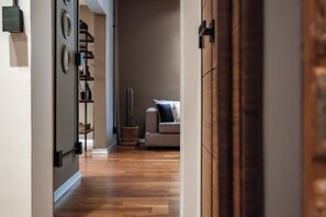 Ein Flur mit Holzboden, der in einen Wohnbereich mit Sofa und Topfpflanze führt.