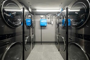 Eine moderne Waschsalon mit drei Waschmaschinen und Trocknern, einem blauen Bedienfeld und einem gefliesten Boden.