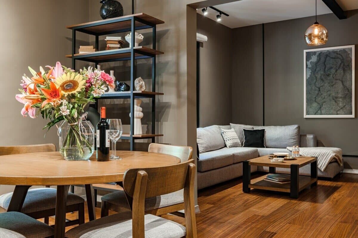 A modern living room with a round wooden dining table, a sofa, and a bookshelf.