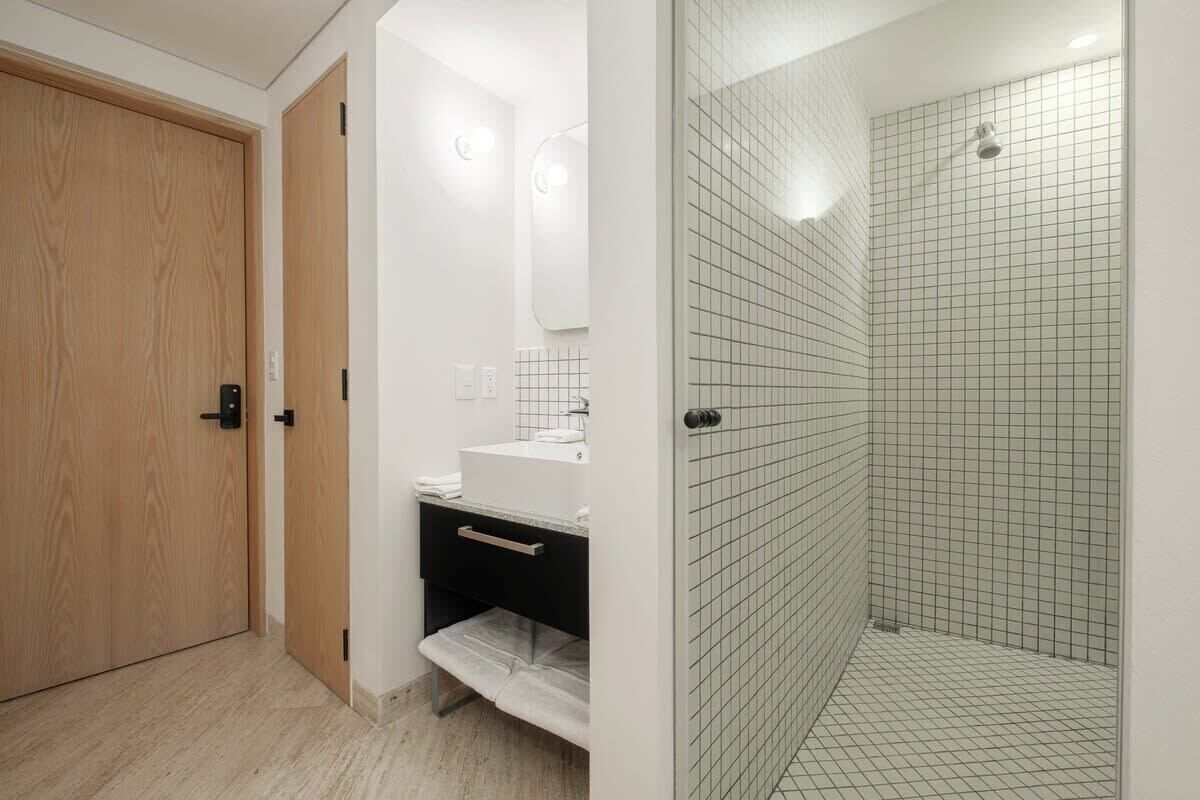 A bathroom with a wooden door, a white sink with a mirror, and a tiled shower area.