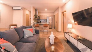 A modern living room with a sofa, a coffee table, a TV, and a kitchen in the background. - Modern flat for 3 in Piantini Gym & pool access (Santo Domingo)