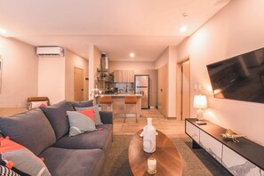 Ein modernes Wohnzimmer mit Sofa, Couchtisch, Fernseher und einer Küche im Hintergrund.