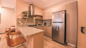 A modern kitchen with a stainless steel refrigerator, granite countertop, and bar stools. - Modern flat for 3 in Piantini Gym & pool access (Santo Domingo)