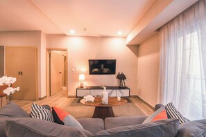A modern living room with a sofa, a coffee table, a TV, and a console table with decorative items. - Modern flat for 3 in Piantini Gym & pool access (Santo Domingo)