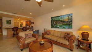 Ein Wohnzimmer mit einer Couch, Sesseln, einem Esstisch, einem Deckenventilator, einem Gemälde und einer Lampe.