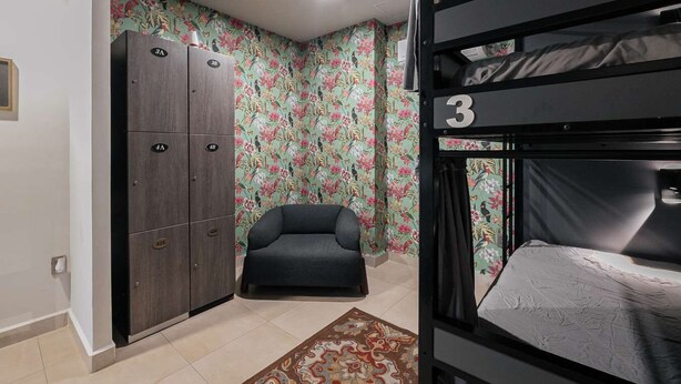 A bunk bed with a number '3' on the side, a grey sofa, a wardrobe with multiple compartments, and a floral wallpaper. - Top Bed | Mixed Shared Room (Ciudad de México)