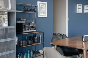 A kitchen with a microwave, shelves with plates and bowls, a table with chairs, and a framed picture on the wall. - Top Bed | Mixed Shared Room (Ciudad de México)