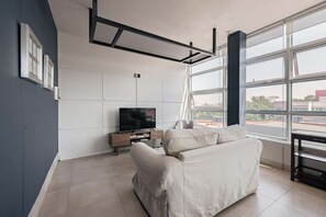 Ein modernes Wohnzimmer mit Flachbildfernseher, einer Couch und einem großen Fenster mit Blick auf die Stadt.